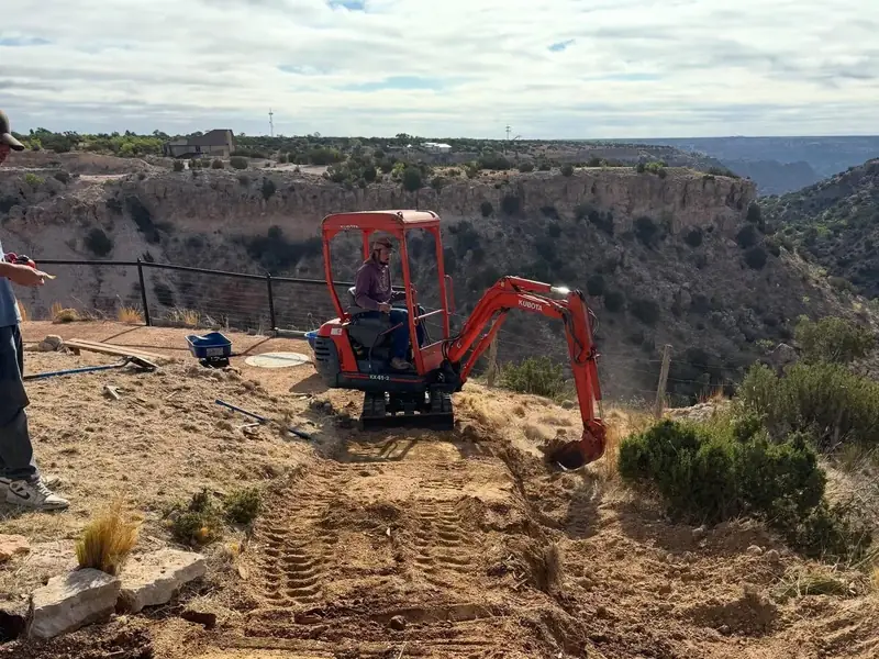 Orange mini excavator trenching along the canyon rim in the Texas Panhandle